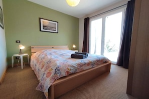Ein Schlafzimmer mit einem Bett, Nachttischlampen, einem Fenster mit Vorhängen und einem gerahmten Bild an der Wand.
