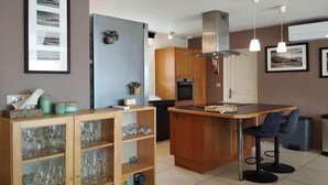 A modern kitchen with a central island, wooden cabinets, and a bar area with stools. - Charming 4-Bedroom House in the Heart of the Lot (LACHAPELLE AUZAC)