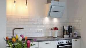 A kitchen with white cabinets, a stove, a coffee maker, and a vase with flowers. - Vacation apartment Geestland "buten un binnen" North Sea (Geestland)