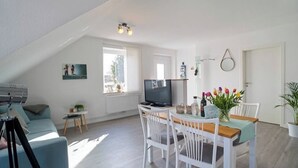 A modern living room with a television, a dining table with chairs, a sofa, and a telescope. - Vacation apartment Geestland "buten un binnen" North Sea (Geestland)
