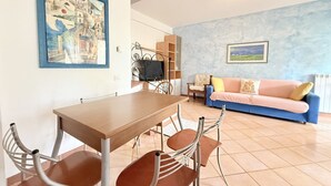 A dining area with a table and chairs, a sofa, a TV, and a painting on the wall. - P086 - Porto Recanati, villa with garden and terrace (Porto Recanati)