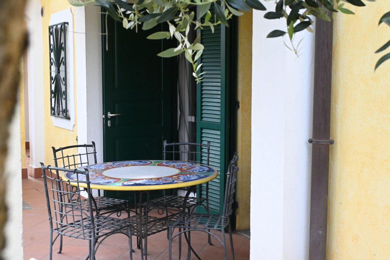 Un patio al aire libre con una mesa redonda y cuatro sillas, una puerta verde y una pared amarilla.
