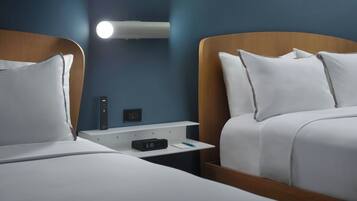 Deux lits avec des têtes de lit en bois, une table de chevet avec une horloge, une télécommande et un luminaire fixé au mur.