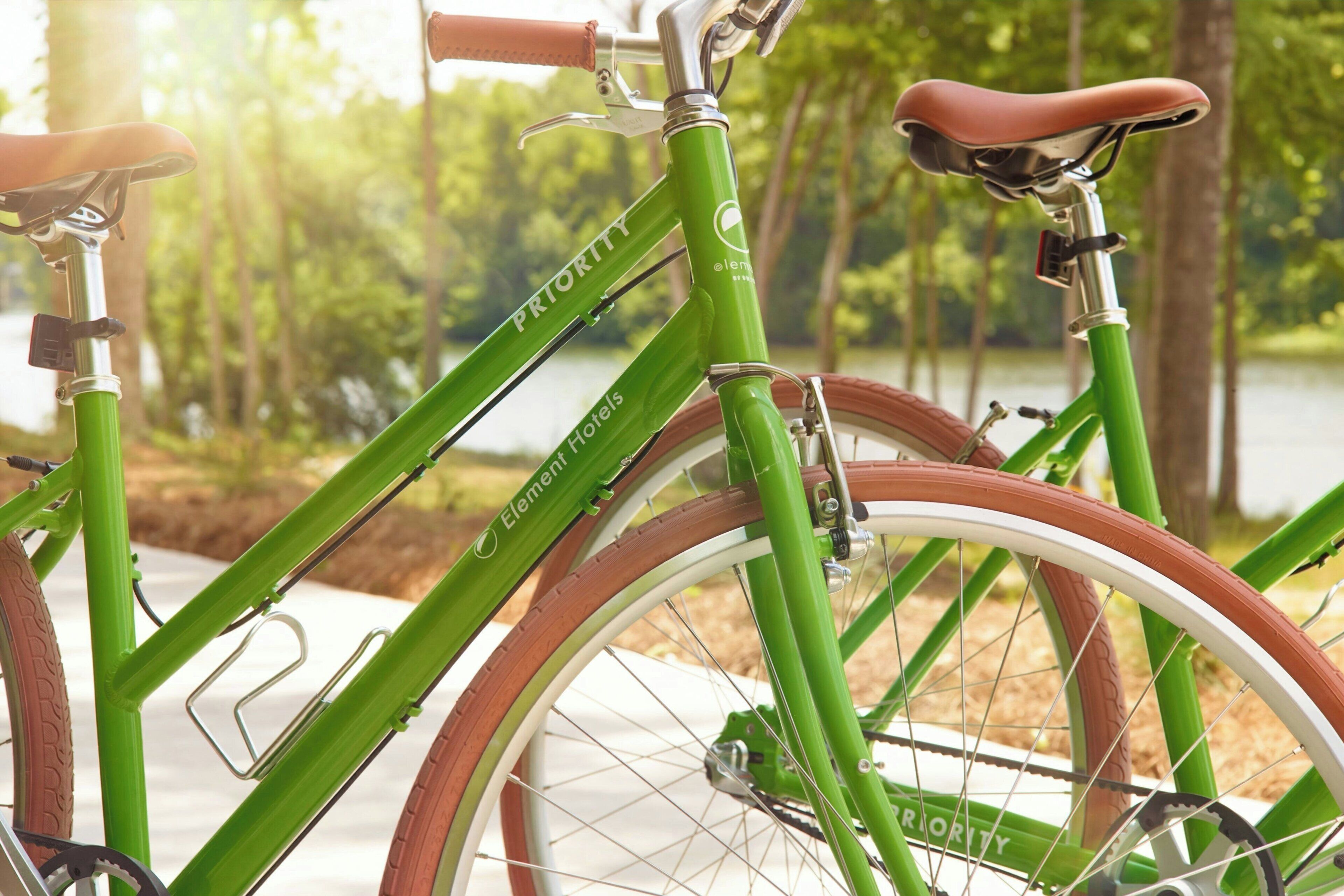 Una bicicleta verde con la leyenda 'PRIORITY' y la marca 'Element Hotels', estacionada cerca del agua.