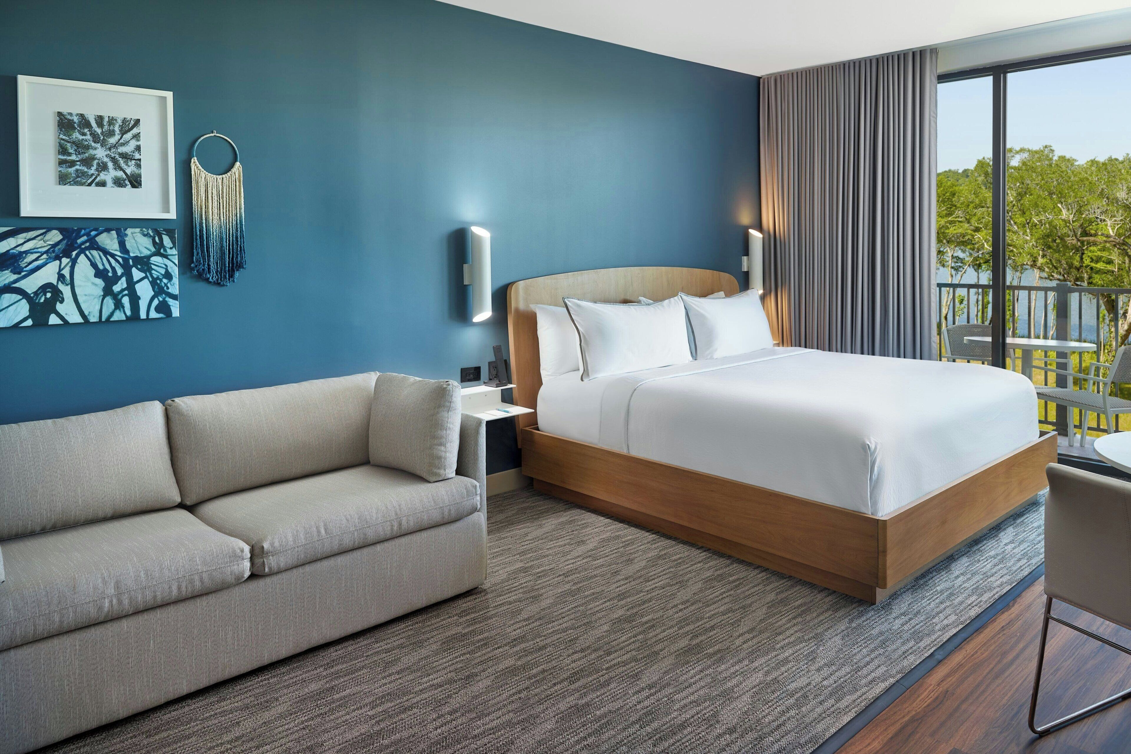 Ein Hotelzimmer mit Bett, Sofa, Nachttisch und Blick ins Freie.