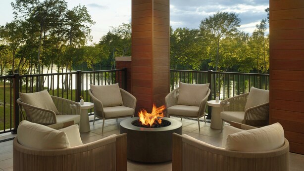A terrace with wicker furniture, a central fire feature, and a view of trees and water. - Element by Marriott Bainbridge Riverfront (Bainbridge)