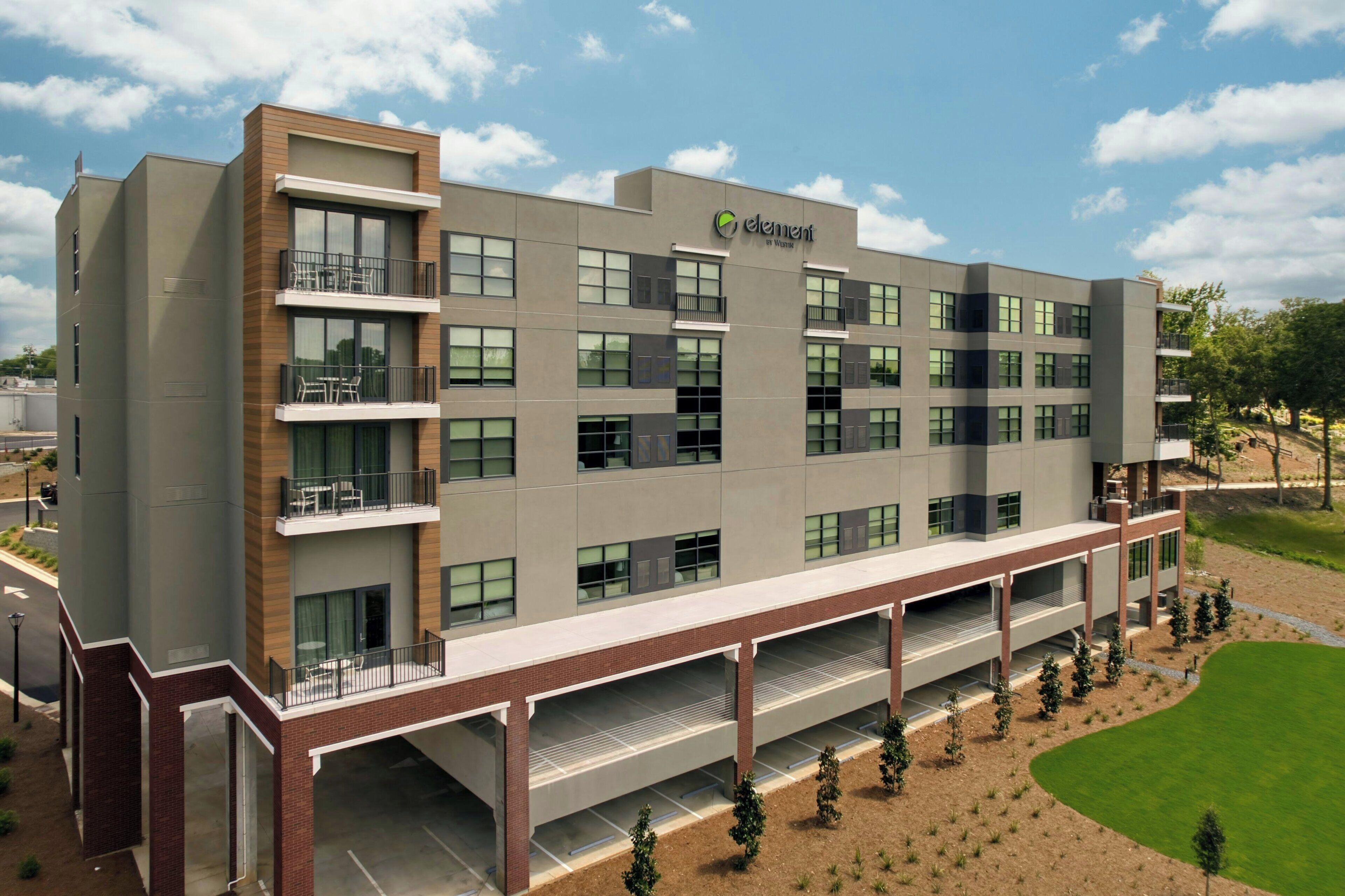 A multi-story hotel with a flat roof, large windows, and a covered outdoor area with a parking lot.