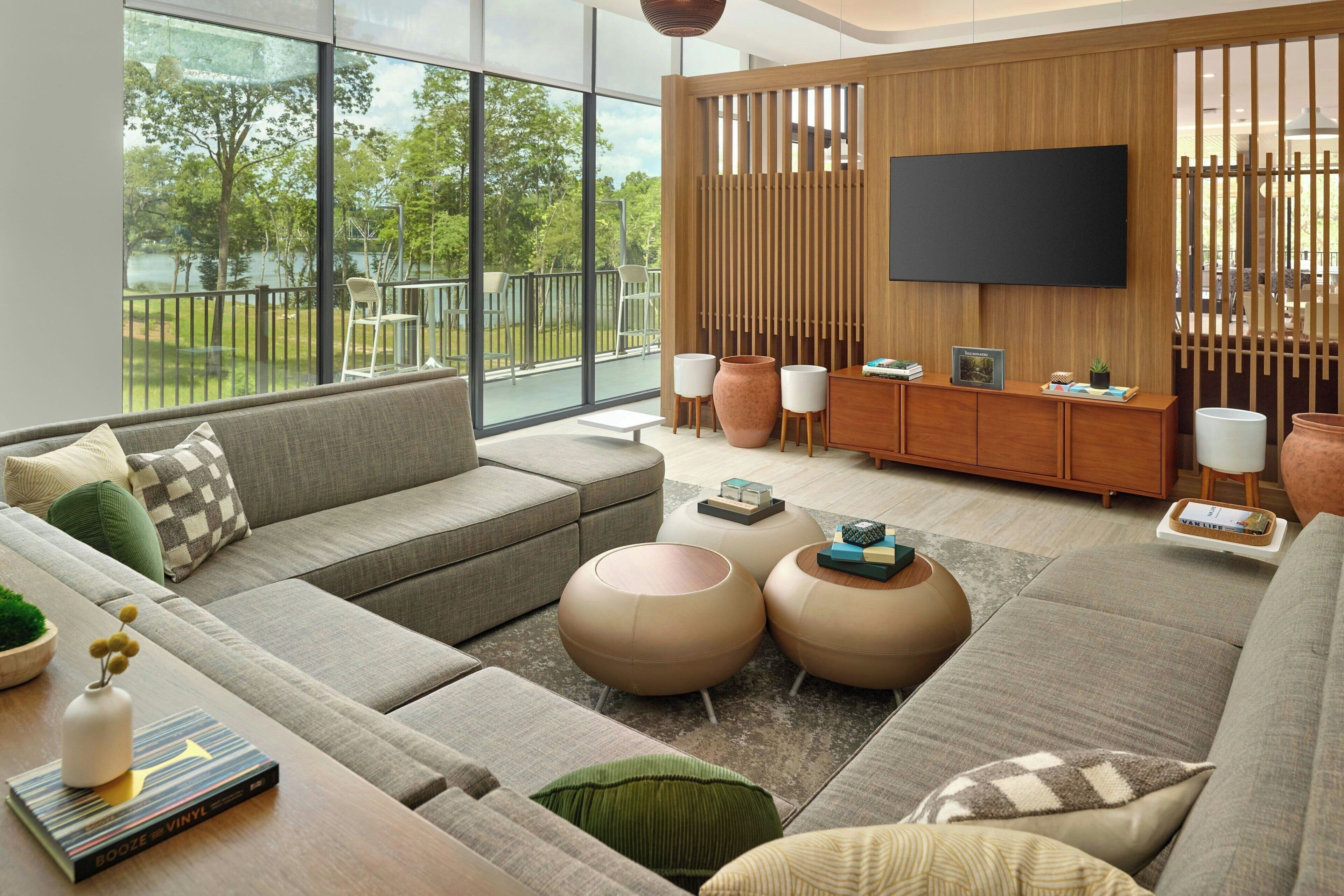 Ein modernes Wohnzimmer mit einer großen Couch, zwei runden Hocker, einem Couchtisch und einem an einer Holzwand montierten Fernseher.