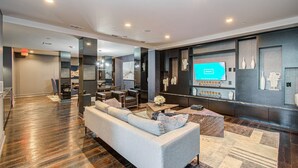 A modern hotel lobby with a sofa, chairs, a TV, and a reception desk. - Home Movie Theatre. Walk to FIFA/NRG/Med Center. 1BDR Highrise (Houston)