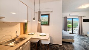 Cocina compacta con lavabo, zona de comedor con mesa y sillas, ventana con vista a zonas verdes y balcón con sofá.