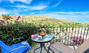 A balcony with a table, chairs, and a view of a hilly landscape.