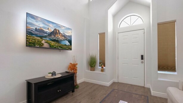 Un intérieur moderne avec un téléviseur fixé au mur, une console sombre, une porte et une fenêtre avec des stores.