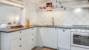Ett kök med vita skåp, diskmaskin, ugn, diskho och en bänkskiva med diverse köksredskap.