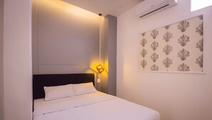 Una cama bien hecha con sábanas blancas, un cabecero negro y un aire acondicionado de pared.