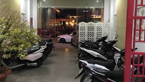 Un área de estacionamiento techada con motocicletas y un coche, una planta en maceta y un separador blanco decorativo.