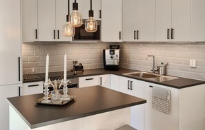 A modern kitchen with white cabinets, a black countertop, a coffee machine, and pendant lights. - 1 bedroom nice home in Torslanda (Torslanda)