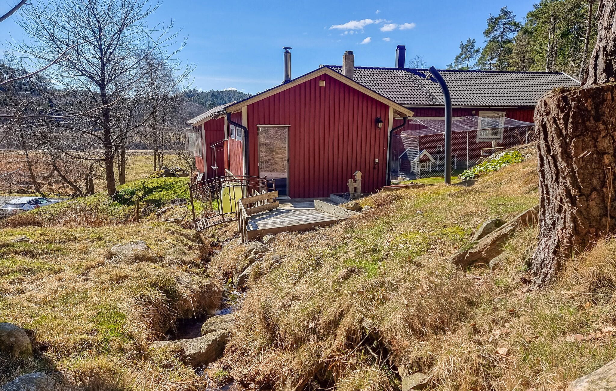 A red wooden cabin with a metal roof, a small porch, and a wooden deck.