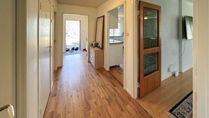Un couloir doté d’un plancher en bois, d’une porte en bois et d’une vue sur une pièce avec une fenêtre.