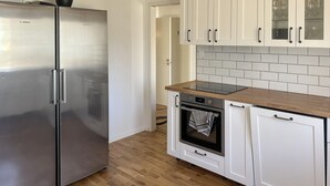 Une cuisine équipée d’un réfrigérateur Bosch en acier inoxydable, d’un plan de travail en bois, de meubles blancs et d’un meuble vitré placé au-dessus du four.