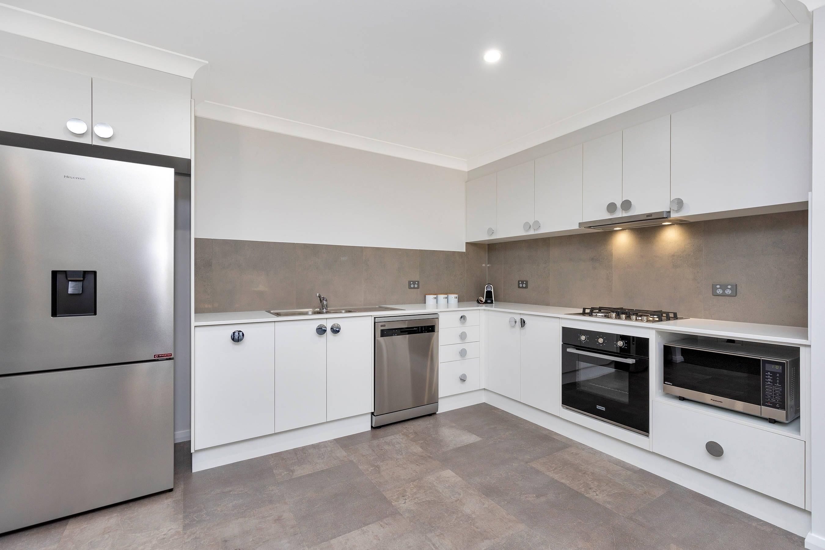 A modern kitchen with stainless steel appliances, white cabinetry, and a tiled backsplash.