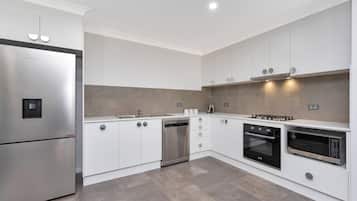 A modern kitchen with stainless steel appliances, white cabinetry, and a tiled backsplash.