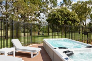 A hot tub on a wooden deck with a white lounge chair, surrounded by a black metal fence and trees. - Plumes a CH Boutique Hotel & Apartments, an Ascend Collection Hotel (TAMWORTH)