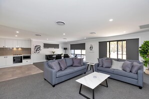 A modern living room with a grey sofa, a coffee table, and a kitchen in the background. - Plumes a CH Boutique Hotel & Apartments, an Ascend Collection Hotel (TAMWORTH)