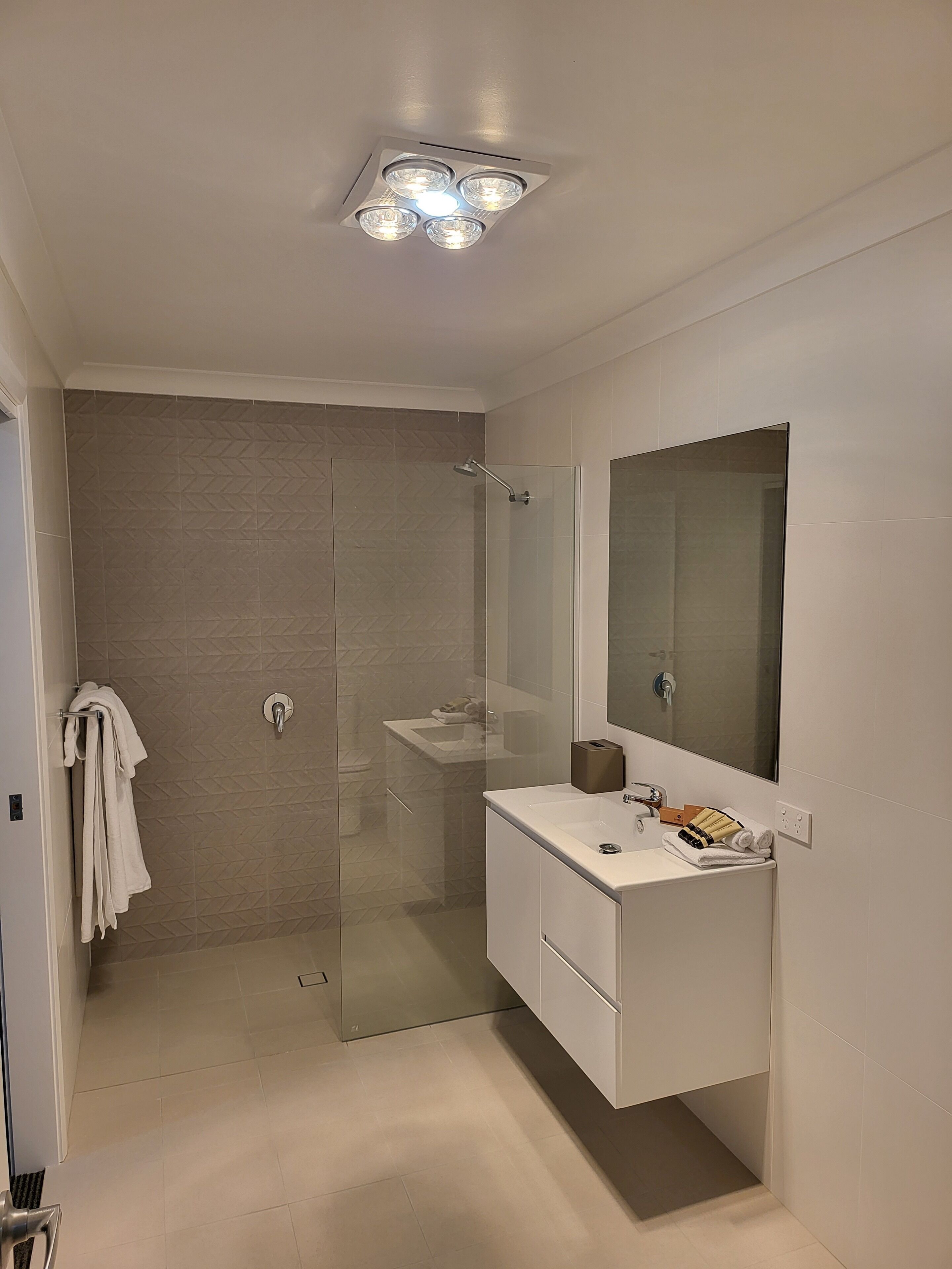 Un baño moderno con ducha envuelta en vidrio, tocador blanco con espejo y lámpara en el techo.