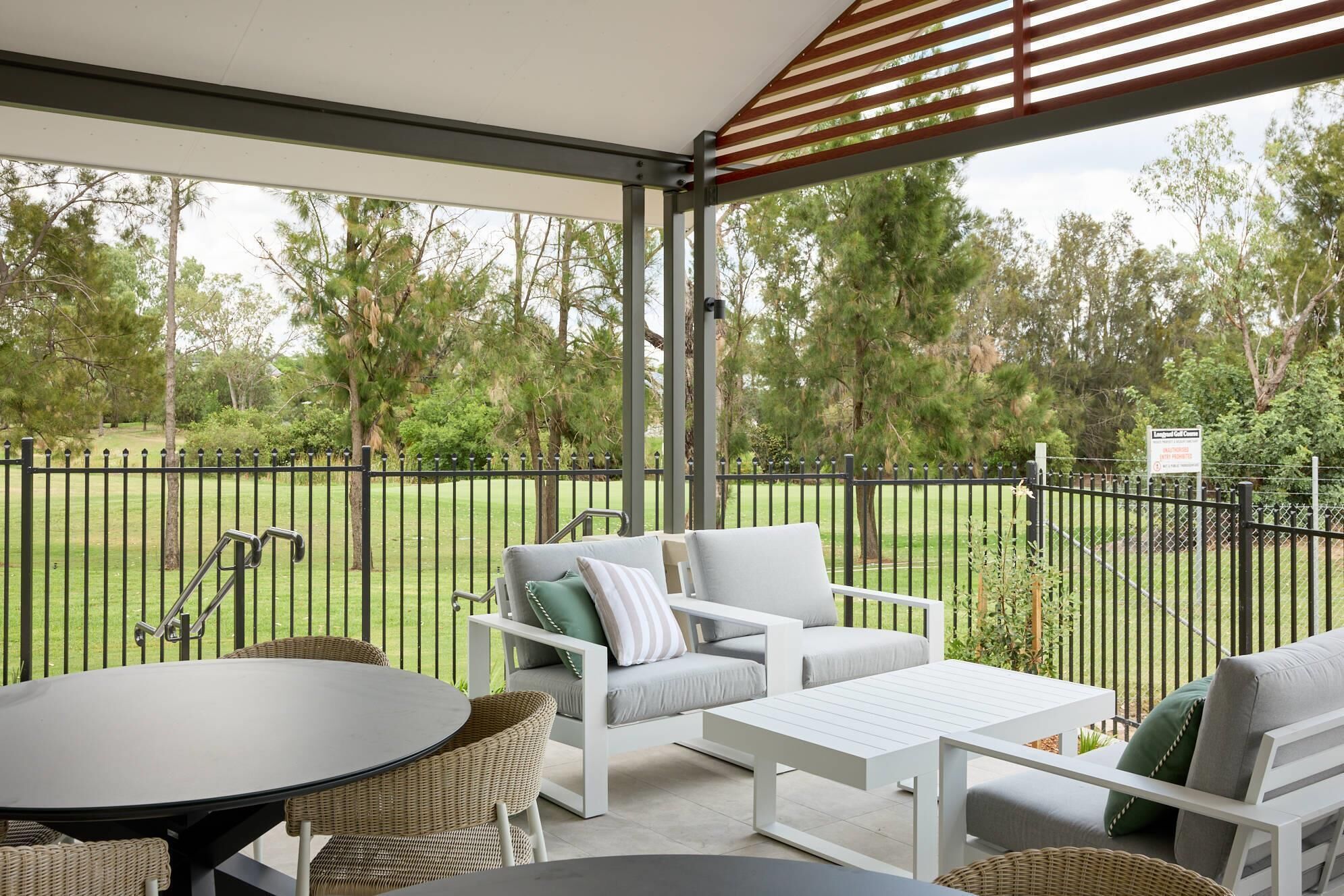 A covered outdoor seating area with wicker furniture, a table, and a view of a lawn and trees.