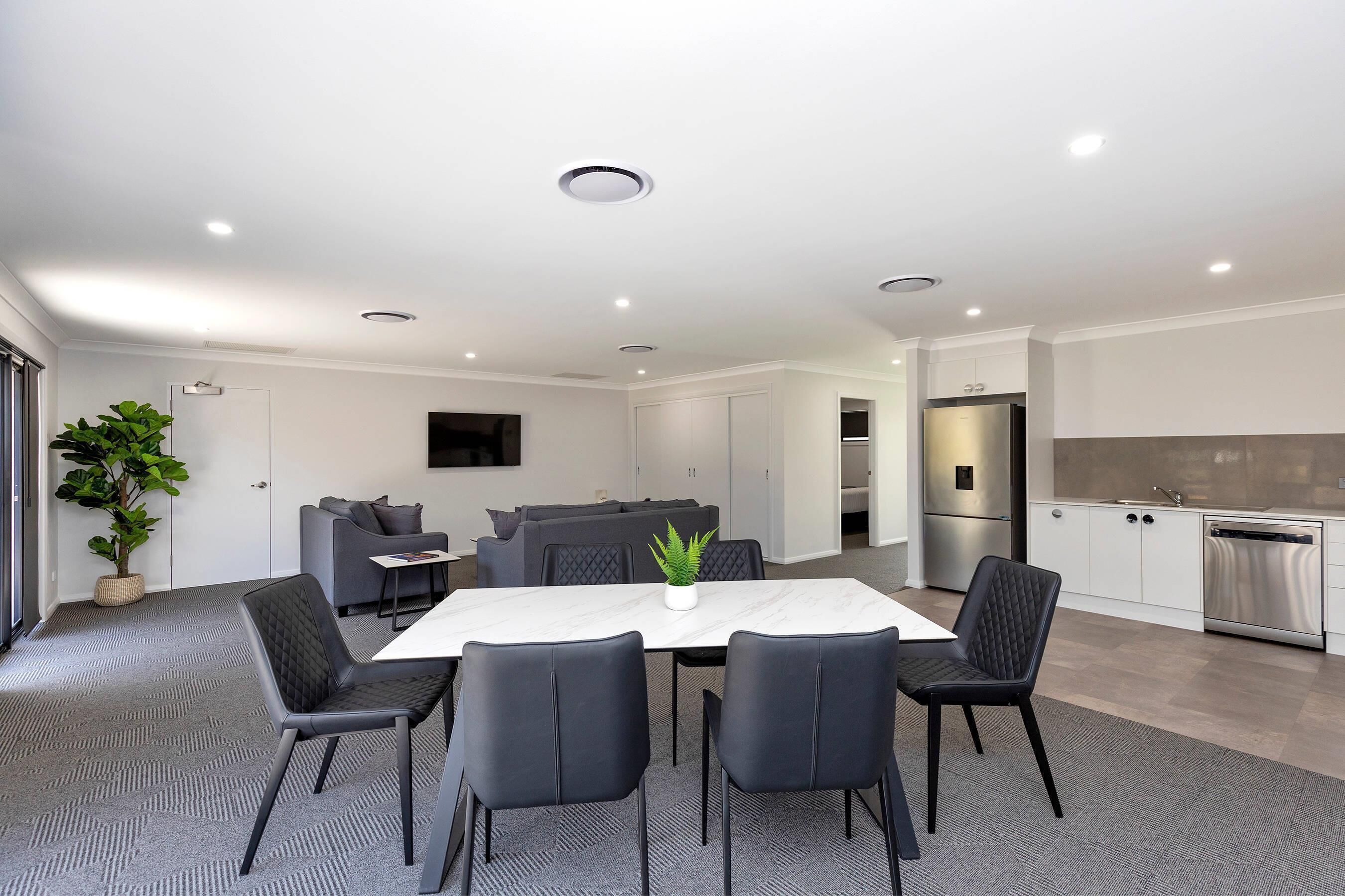 A modern kitchen with white cabinets, stainless steel appliances, and a dining area with a marble table and black chairs.
