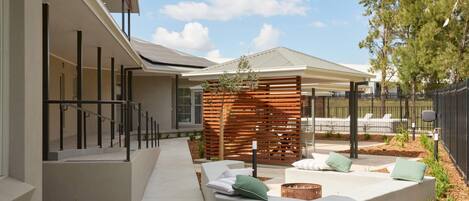 A modern outdoor patio area with a concrete pathway, wooden slatted privacy screen, and outdoor seating with cushions.