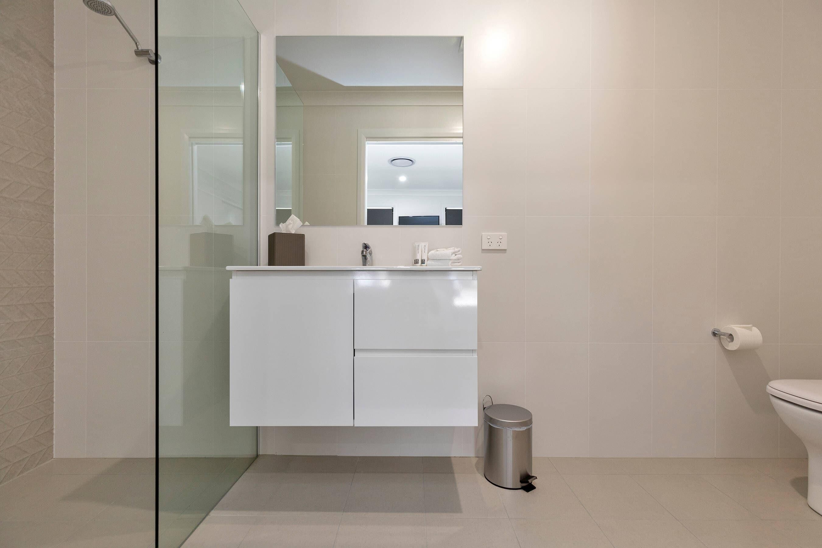 A modern bathroom with a glass shower enclosure, a white vanity with a mirror, and a toilet.