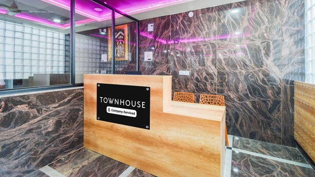 En receptionsdisk med teksten 'TOWNHOUSE', en marmorvæg og et loft med lilla belysning.