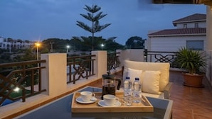 Un balcon avec une table dressée pour deux personnes, une cafetière et deux bouteilles d’eau.