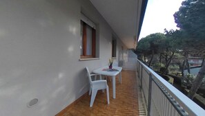 Ein Balkon mit Tisch und Stühlen, ein Fenster und Blick auf Bäume.