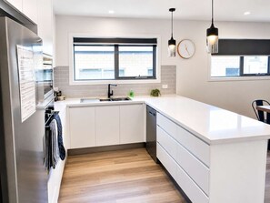 A modern kitchen with white cabinetry, a large island, a window with a view, and pendant lighting. - NEW "Sassafras Villa" No3 | 10 Min City/Airport. (Warrane)