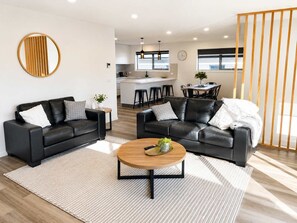 A modern living room with two black leather sofas, a wooden coffee table, and a kitchen in the background. - NEW "Sassafras Villa" No3 | 10 Min City/Airport. (Warrane)