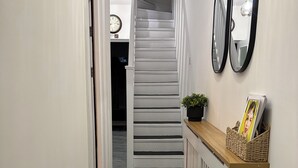 A hallway with a staircase, a radiator, and a wall-mounted mirror. - Modern 4BR Home | Walk to Station | Sleeps 9
Minute from Tottenham Stadium (London)