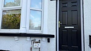 A house with a white exterior, a black door, and a window with a white frame. - Modern 4BR Home | Walk to Station | Sleeps 9
Minute from Tottenham Stadium (London)