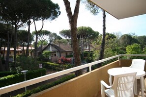 Ein Balkon mit weißen Plastikstühlen und Blick auf ein Wohngebiet mit Häusern und Bäumen.