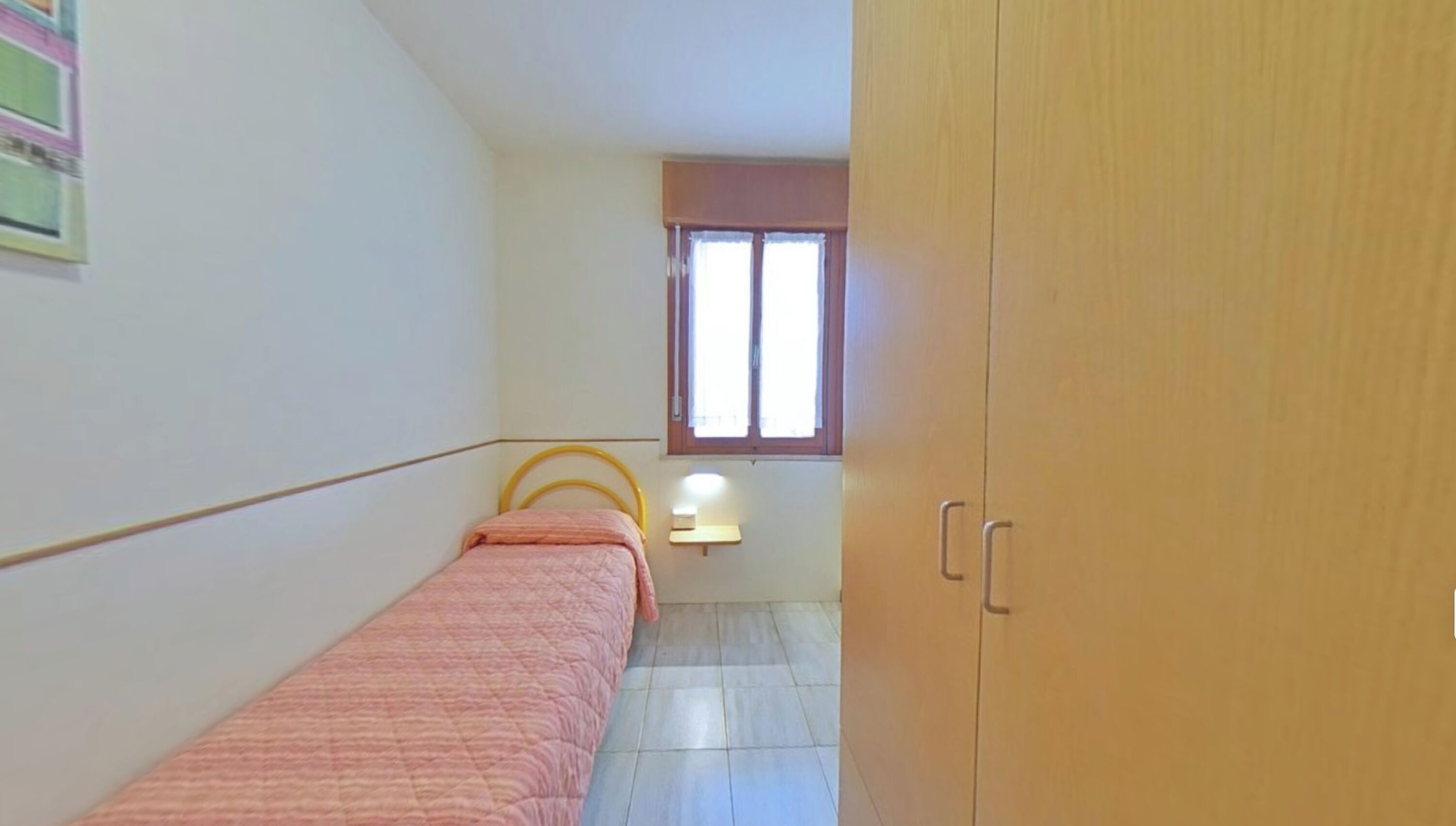 Ein Schlafzimmer mit einem Einzelbett, einem Fenster, einem Nachttisch und einem Kleiderschrank.