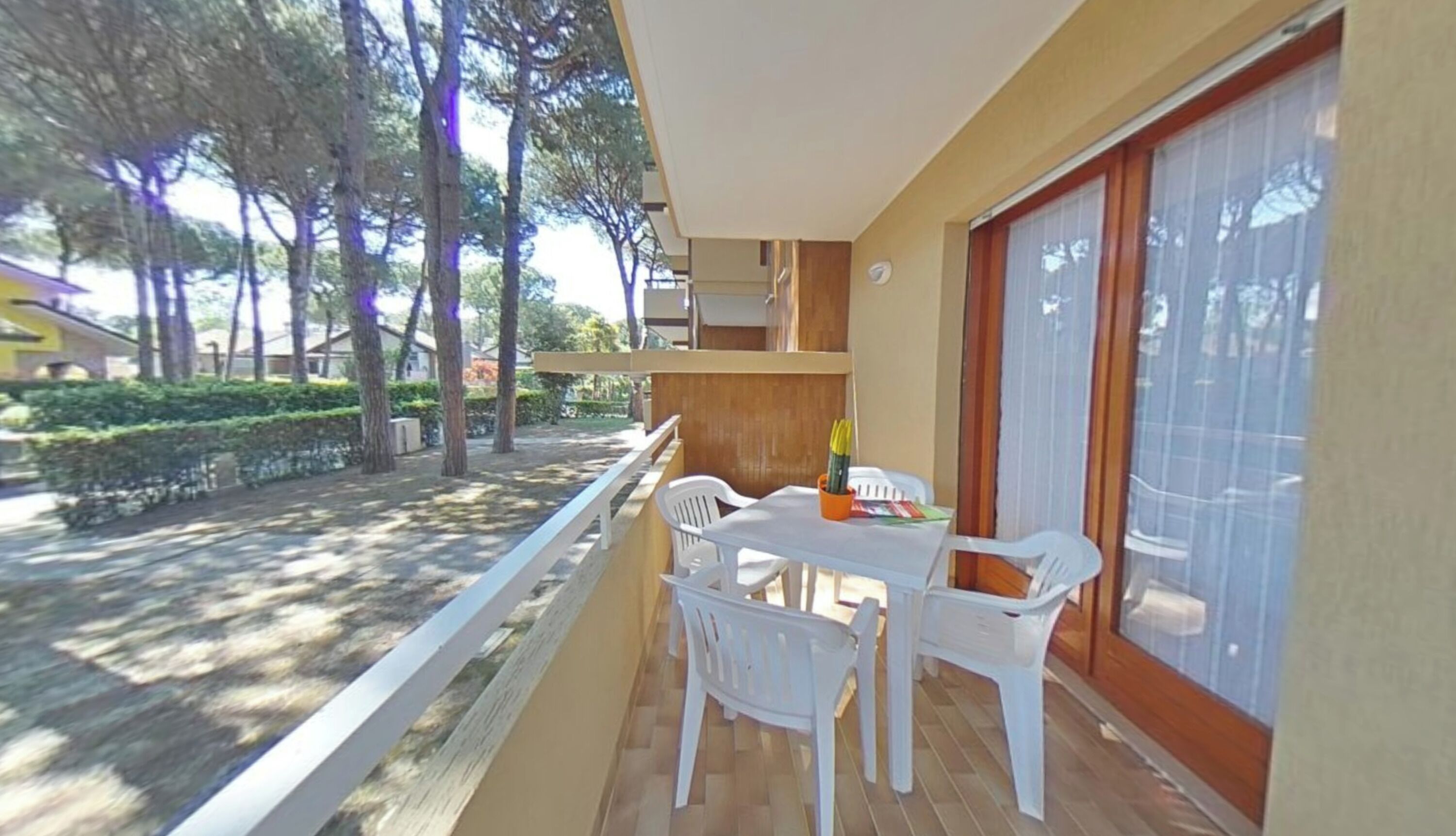Een balkon met een tafel en stoelen, een schuifdeur en uitzicht op bomen en een gebouw.