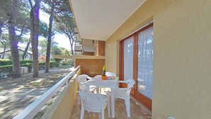 A balcony with a table and chairs, a potted plant, and a view of trees and a building. - Inviting retreat in a relaxing area (Lignano Sabbiadoro)