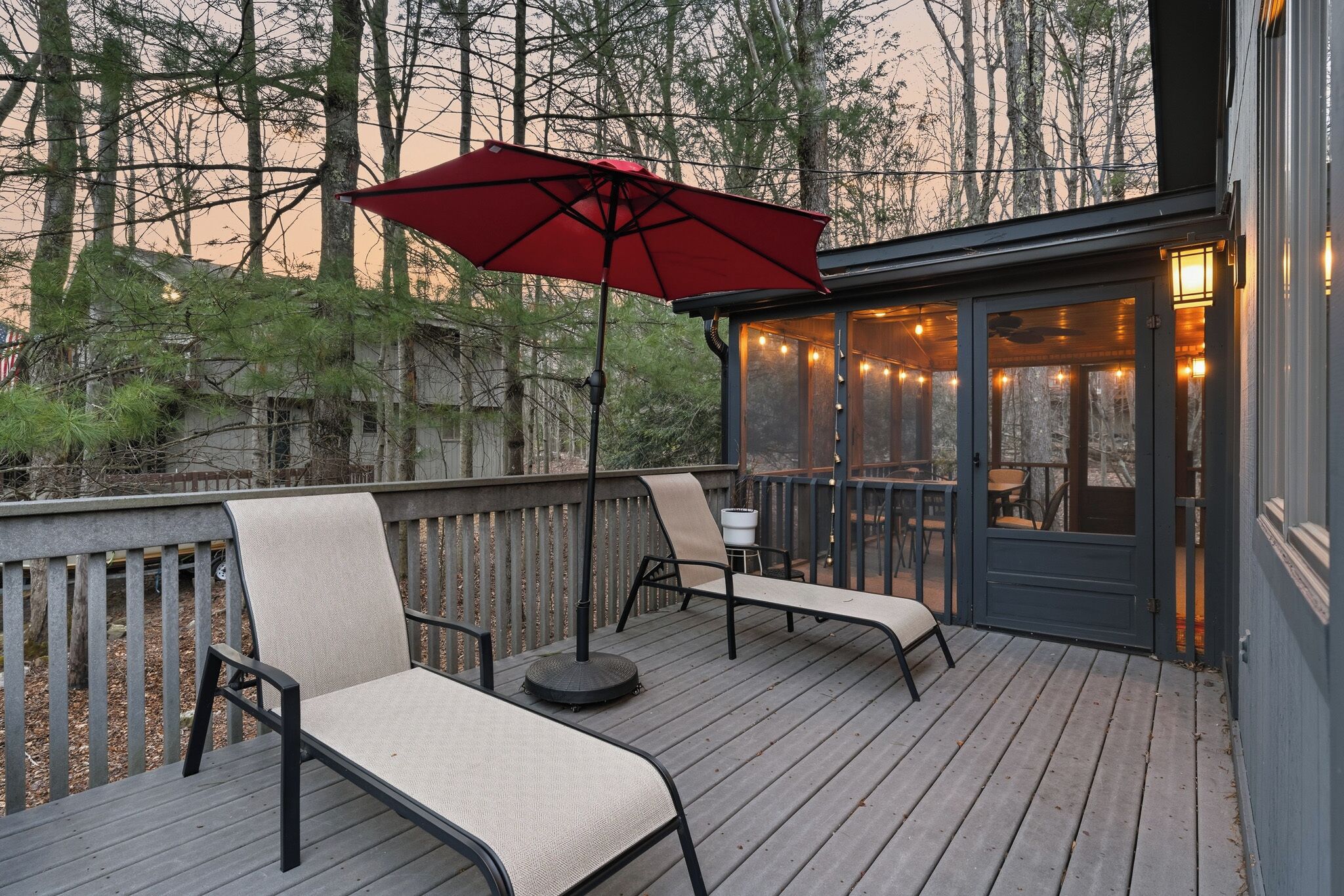 Une terrasse avec deux chaises longues, un parasol rouge et des guirlandes lumineuses.