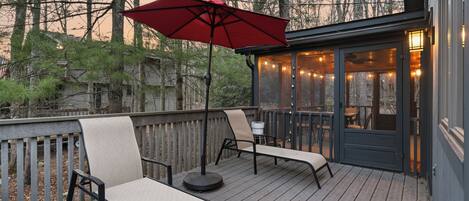 Une terrasse avec deux chaises longues, un parasol rouge et des guirlandes lumineuses.