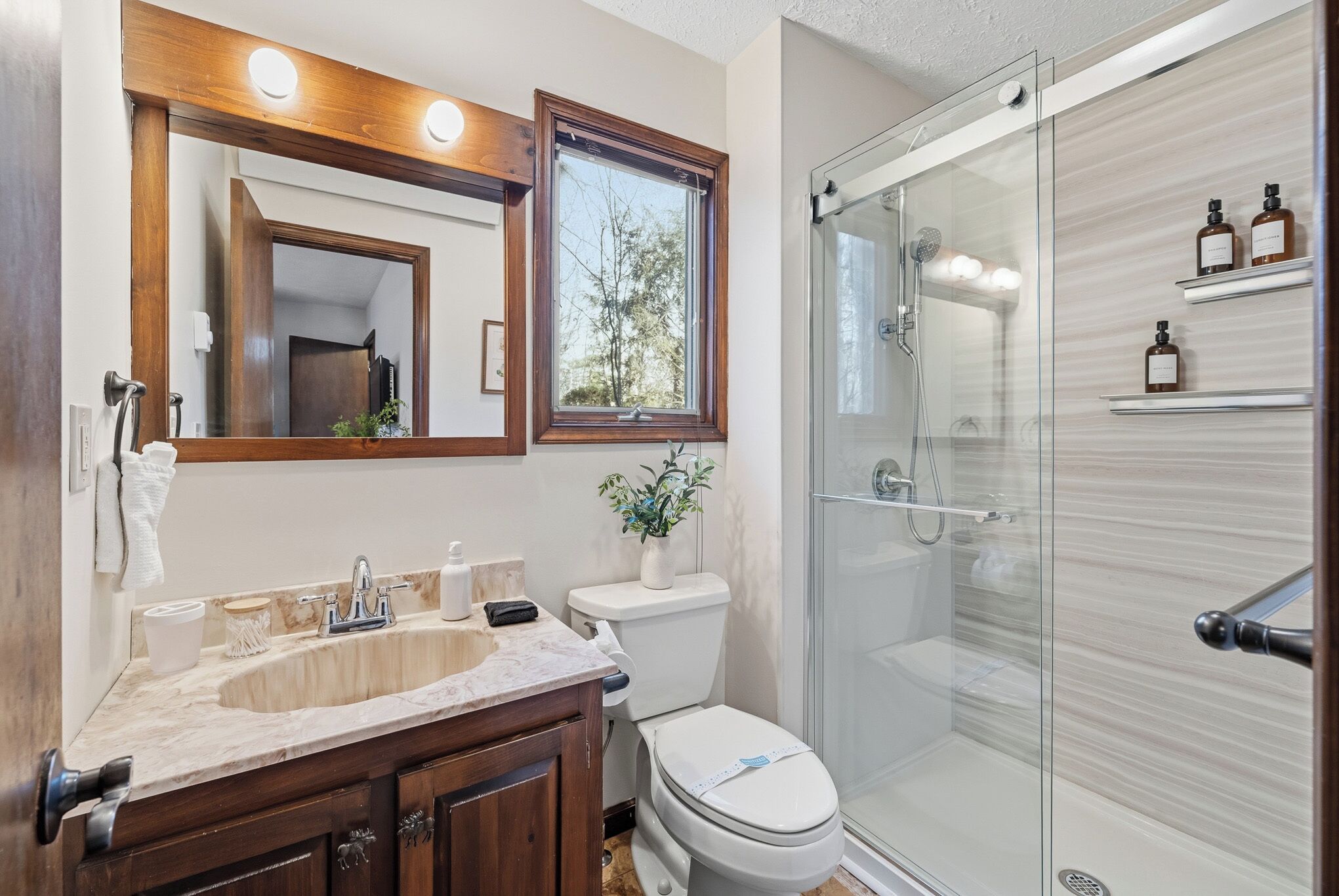A bathroom with a wooden vanity, a large mirror, a toilet, and a glass-enclosed shower.