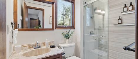 A bathroom with a wooden vanity, a large mirror, a toilet, and a glass-enclosed shower.