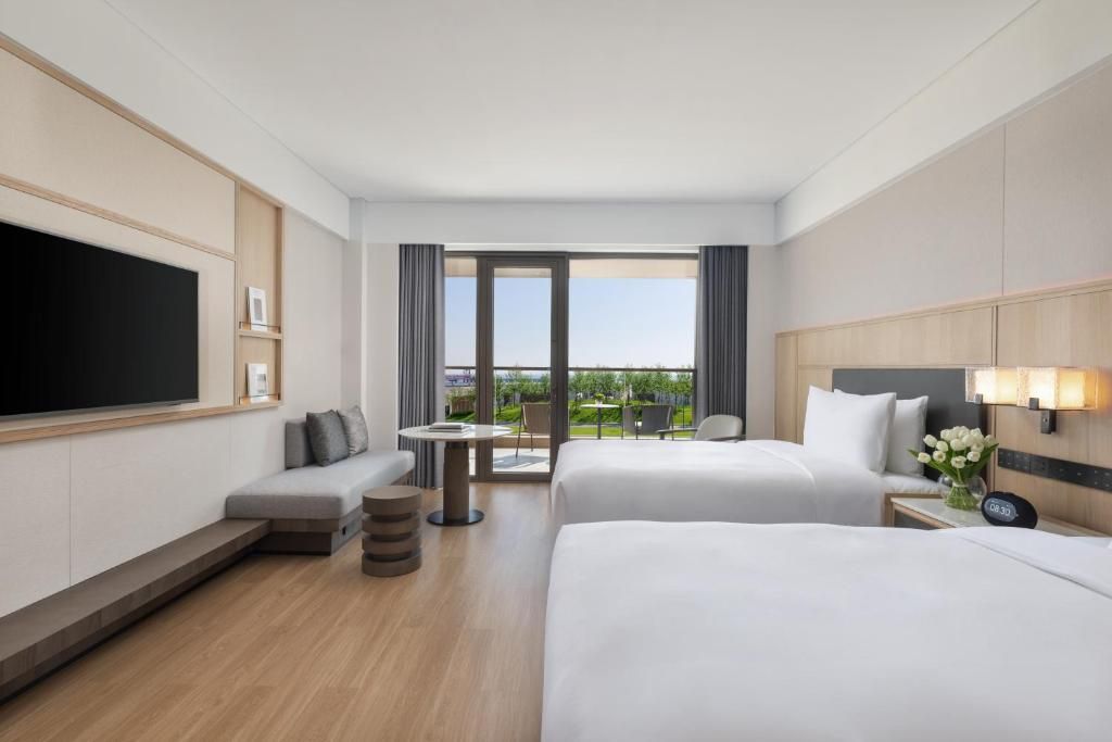 Una habitación de hotel con una cama grande, una cama más pequeña, un sofá, un televisor, un escritorio y un balcón con vistas.