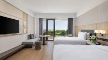 A hotel room with a large bed, a smaller bed, a sofa, a TV, a desk, and a balcony with a view.