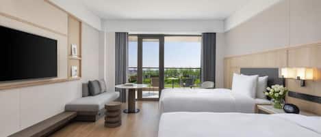 A hotel room with a large bed, a smaller bed, a sofa, a TV, a desk, and a balcony with a view.